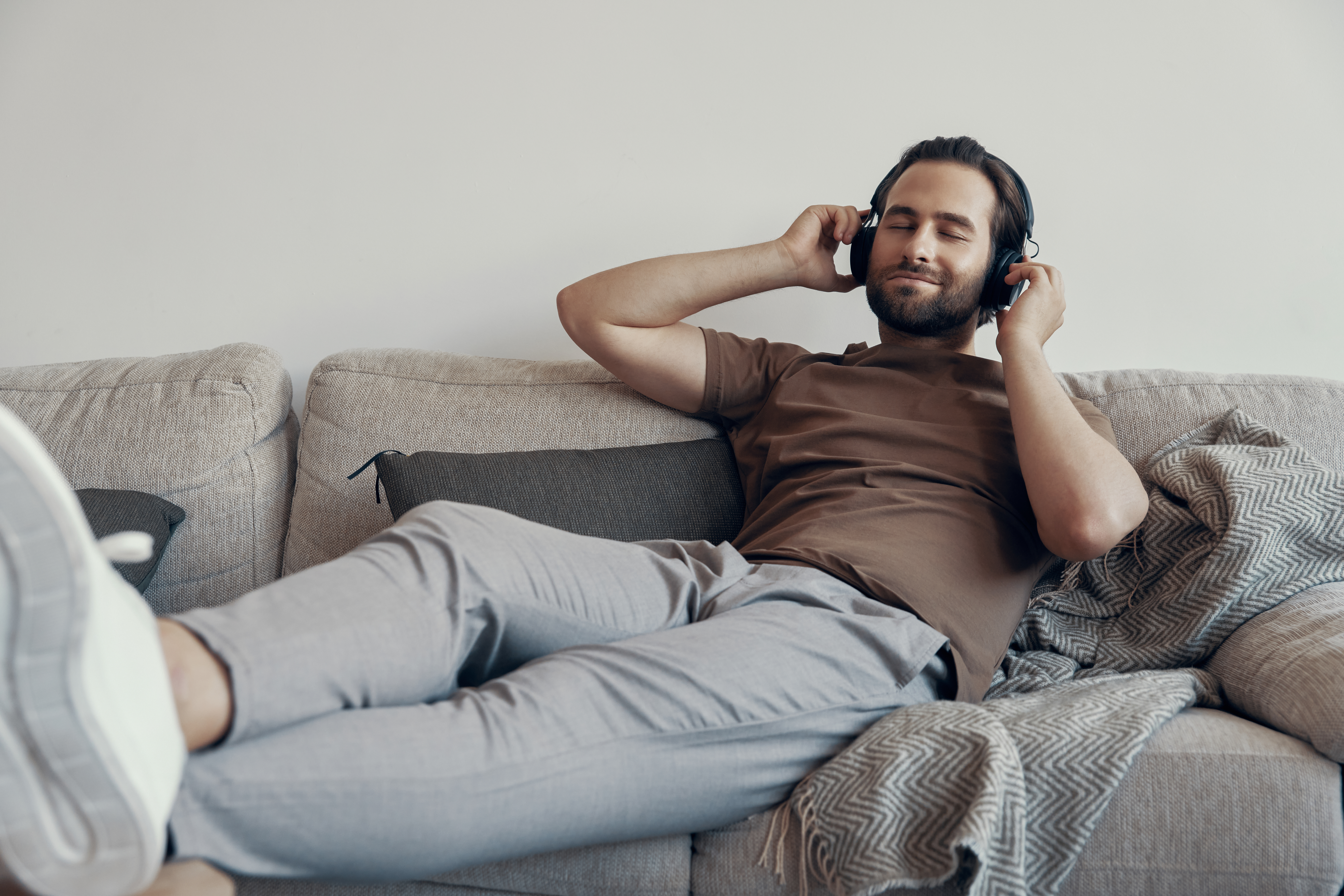 Handsome young man adjusting his headphones while relaxing on the couch at home