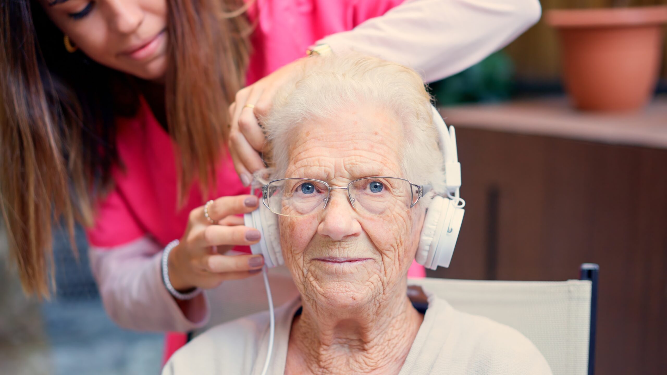 Photo of a nurse adjusting headphones to a senior woman in a geriatric