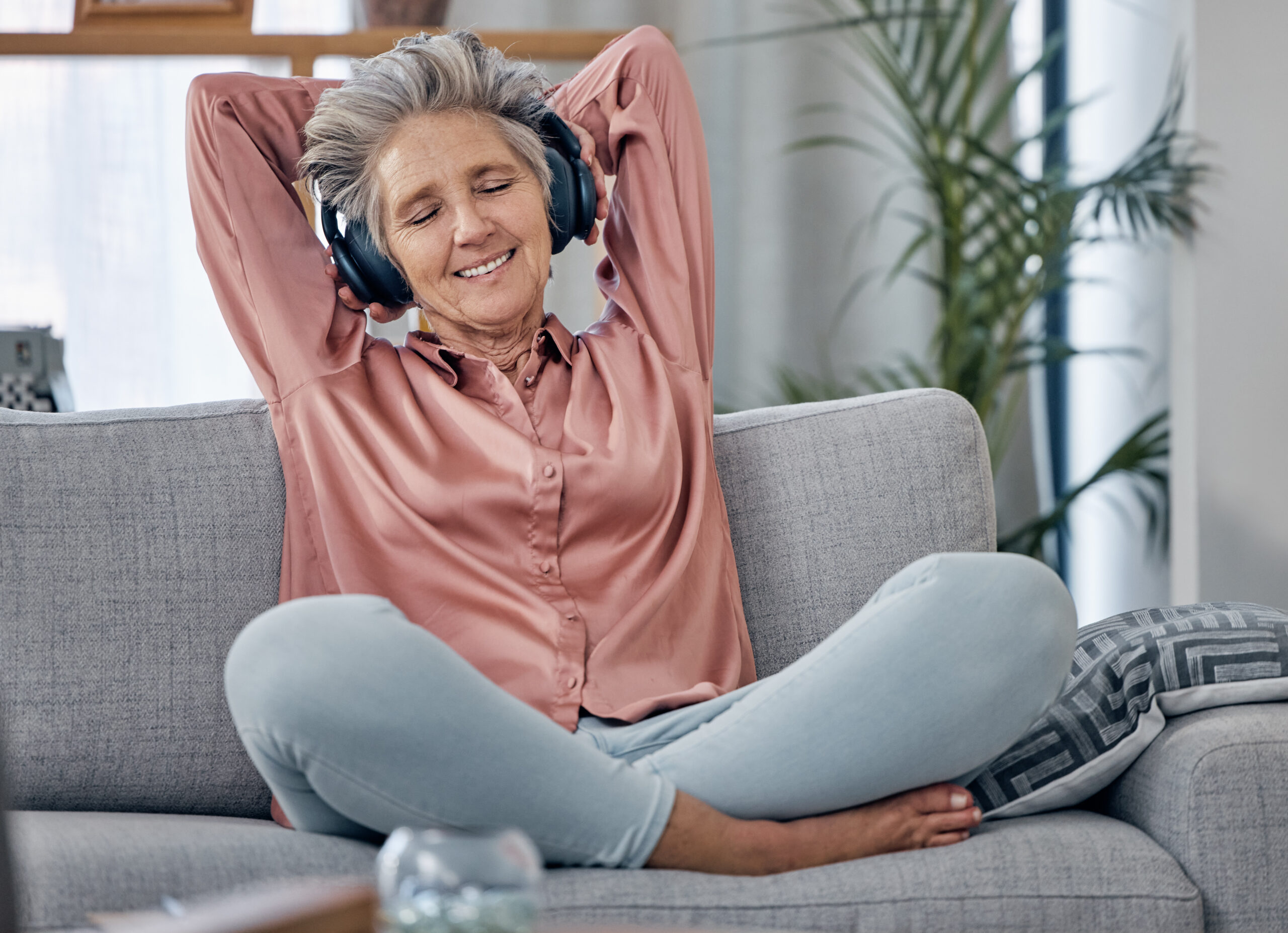 Relax, music and headphones with old woman on sofa for peace, wellness and streaming. Mobile radio,.