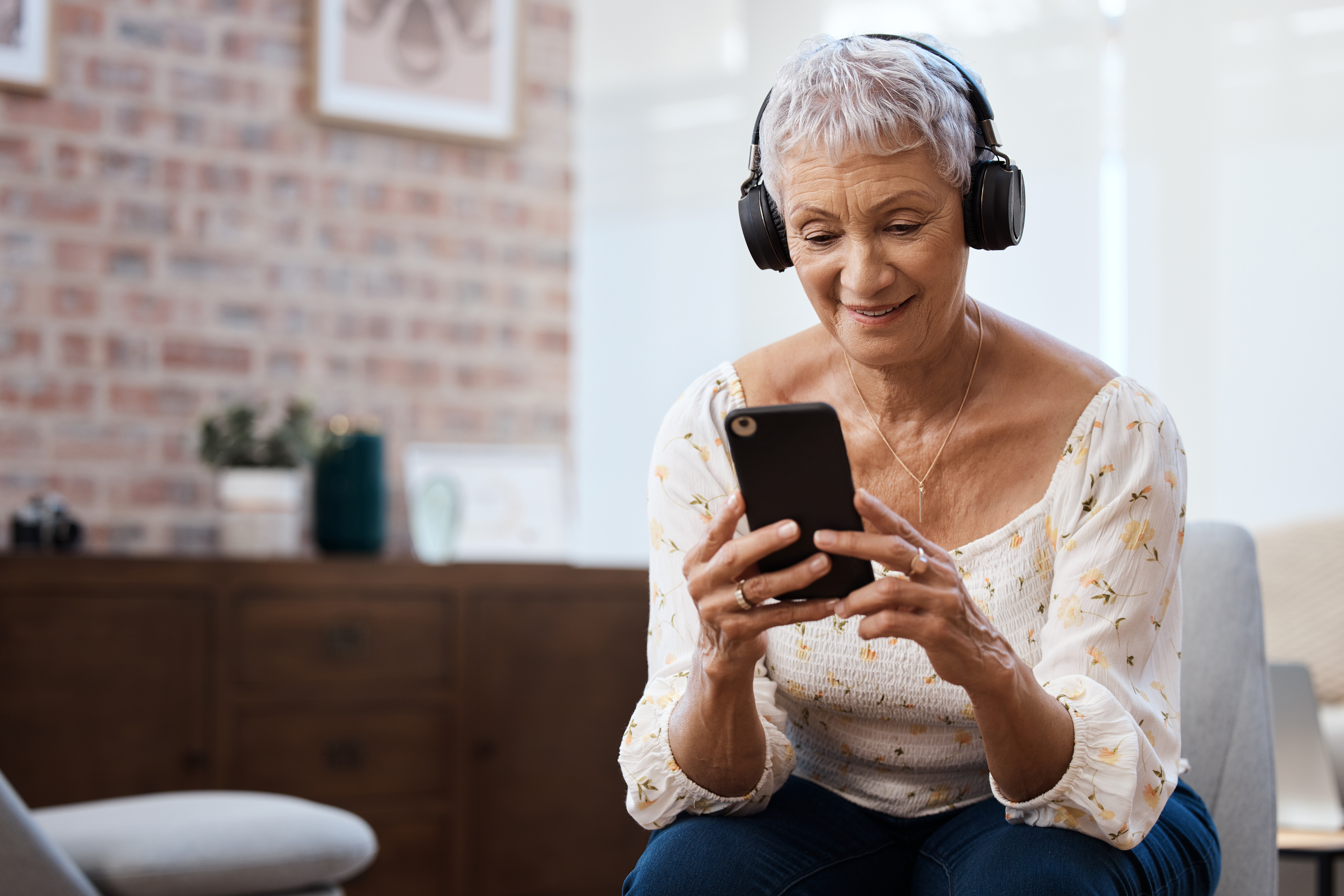 Shot of a senior woman using a smartphone and headphones on the sofa at home.