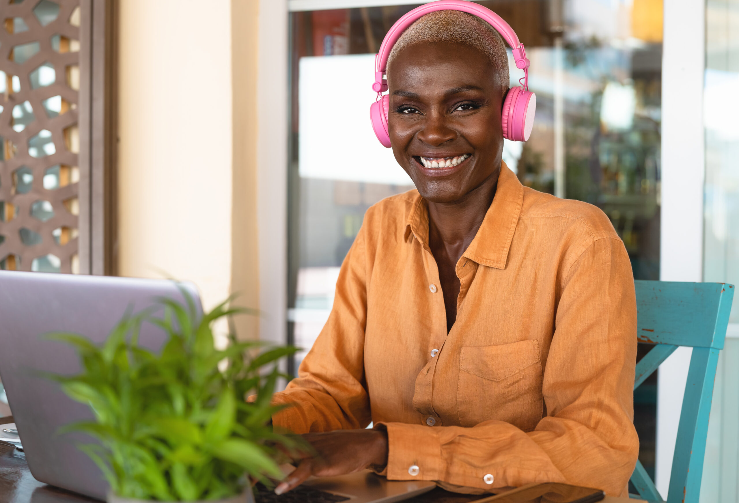 Smiling African woman using laptop and listening music with headphones in bar restaurant - Digital nomad and freelance lifestyle concept