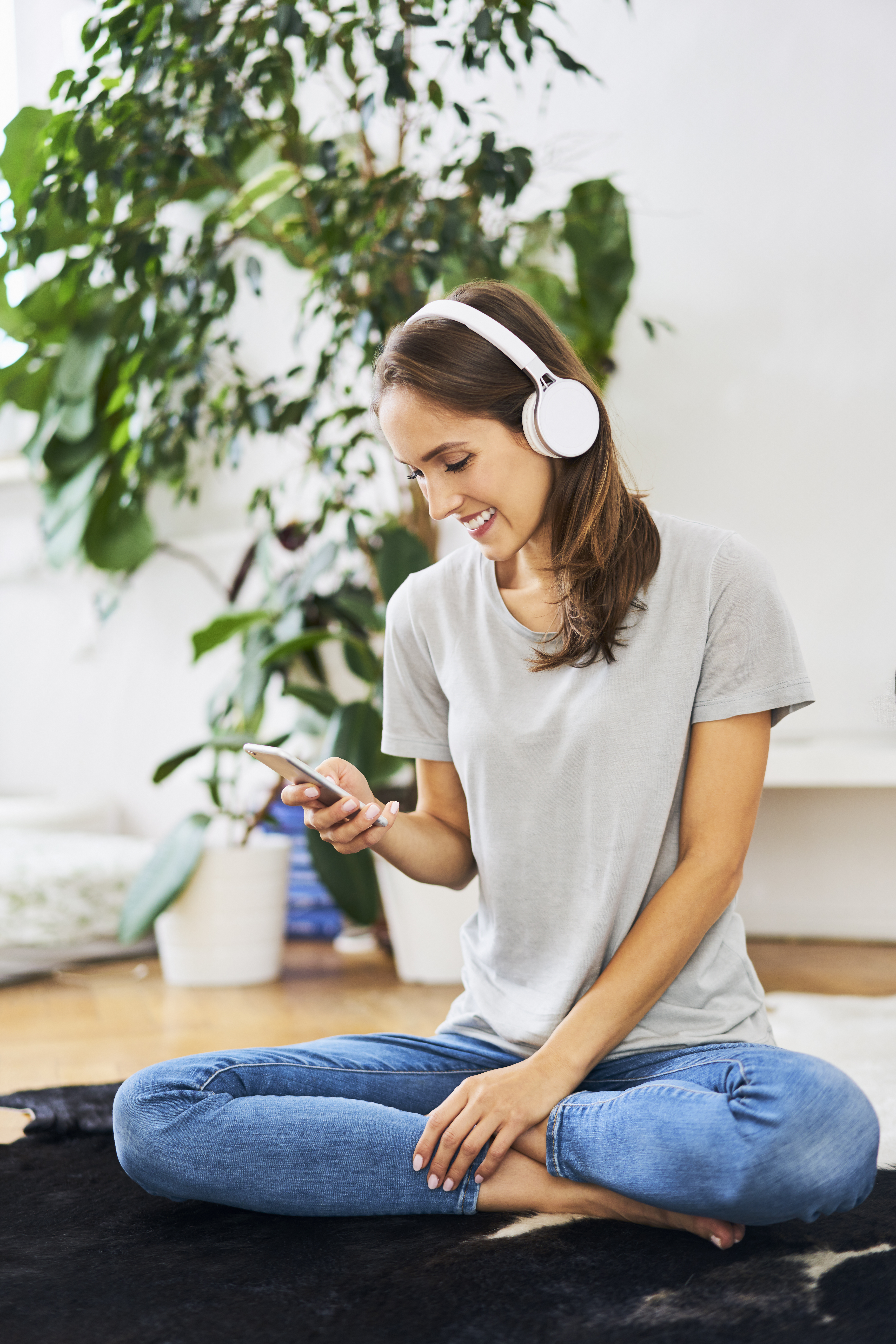 Smiling young woman sitting on the floor with headphones and cell phone