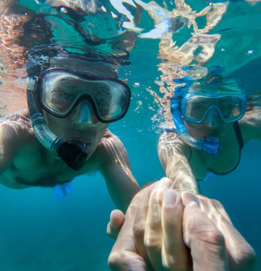 Underwater view of a couple snorkeling and holding hands in tropical ocean