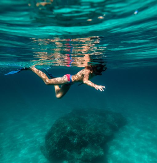 Side view of full body anonymous teenage boy floating in deep blue seawater in flippers and snorkeling mask