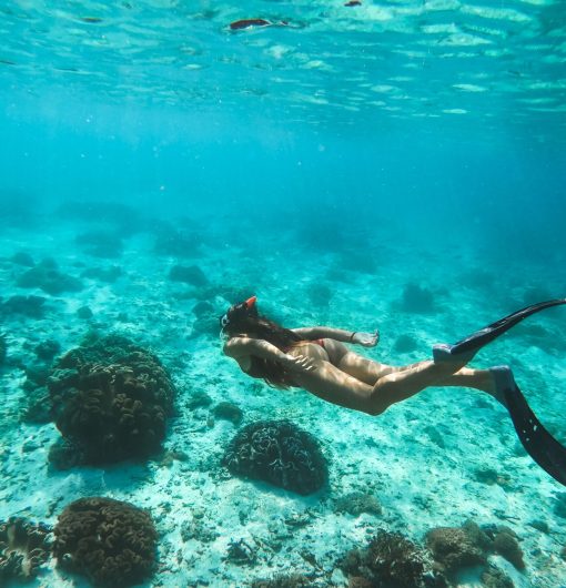 Woman snorkelling underwater with snorkel mask in clear transparent water in beautiful tropical lagoon with coral reef. Freediving activity. Leisure on vacations.